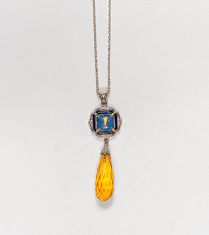 A silver pendant necklace featuring a square blue enamel medallion with a gold Roman numeral 'I' and a faceted amber-yellow teardrop crystal drop, shown against a plain white background.